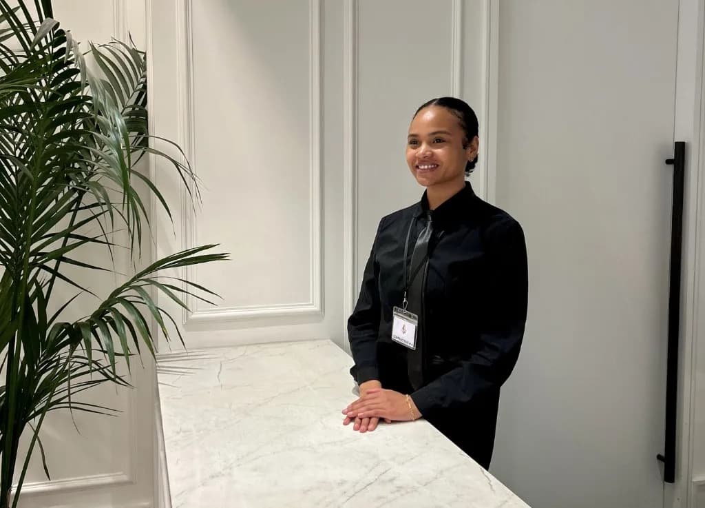 Une receptionniste d'hotel debout derriere un comptoir de reception en marbre